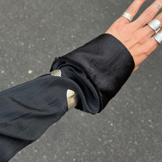Hand wearing multiple rings with a black sleeve against a gray background