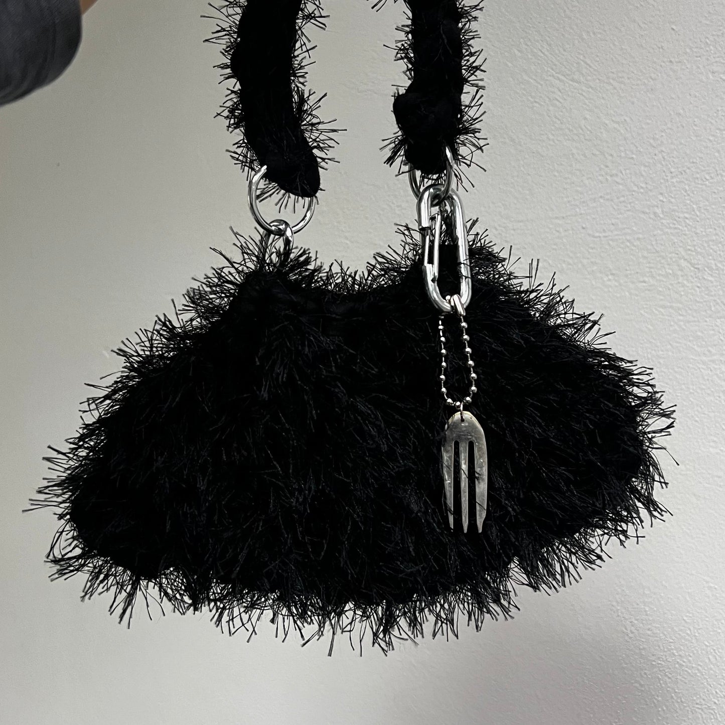 Black textured handbag with chain handle held by a person against a plain background