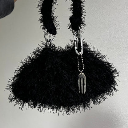 Black textured handbag with chain handle held by a person against a plain background