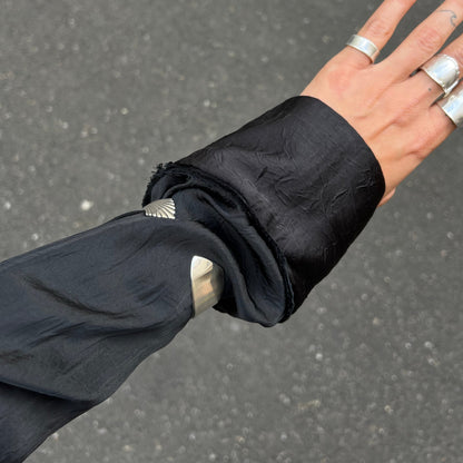 Hand wearing multiple rings with a black sleeve against a gray background