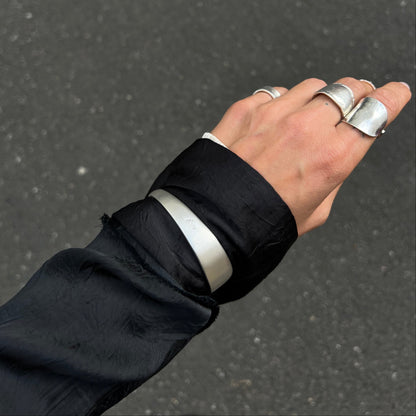 Hand wearing multiple silver rings with a black sleeve against a dark background