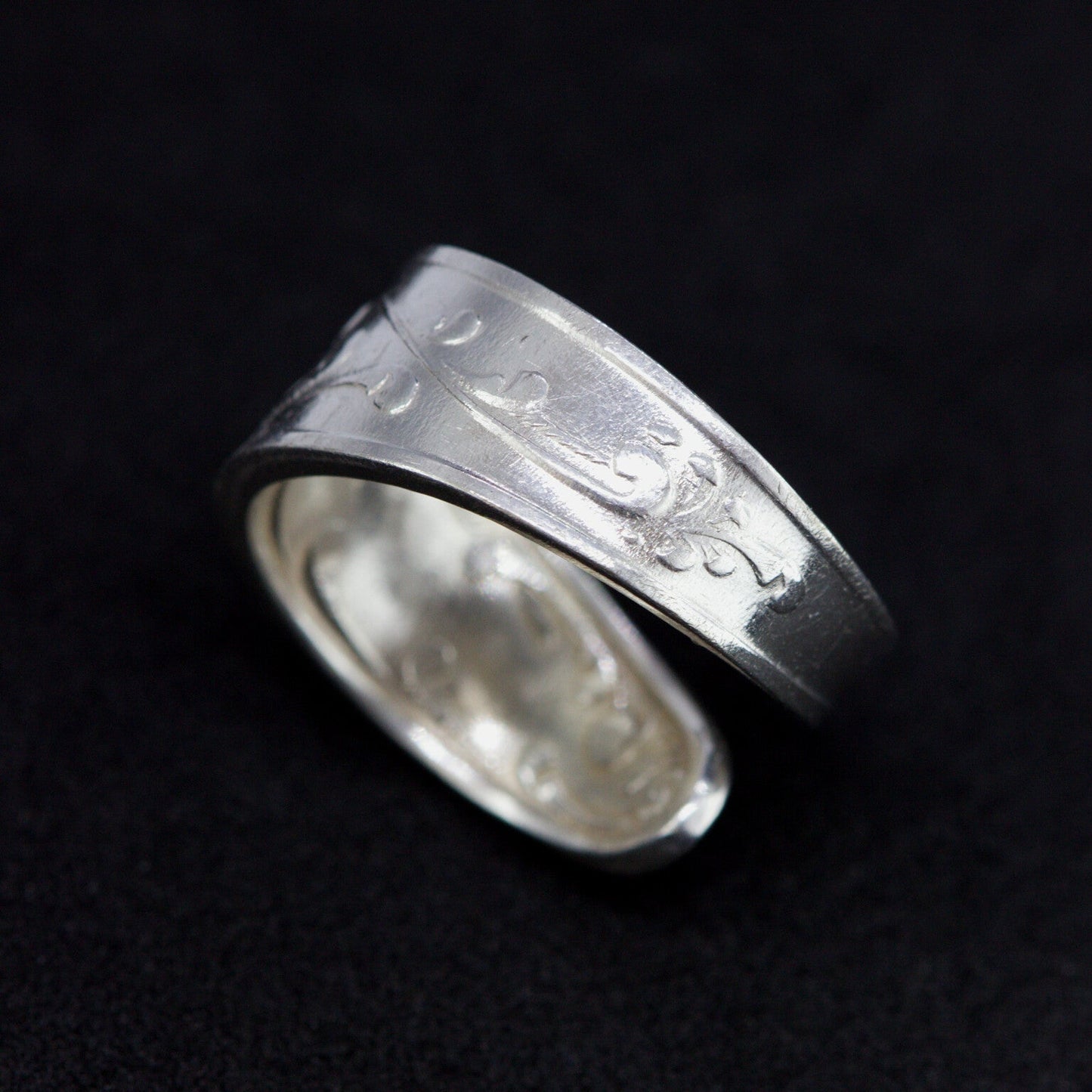 Silver ring with engraved design on a black background