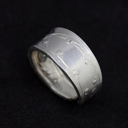 Silver ring with engraved design on a black background