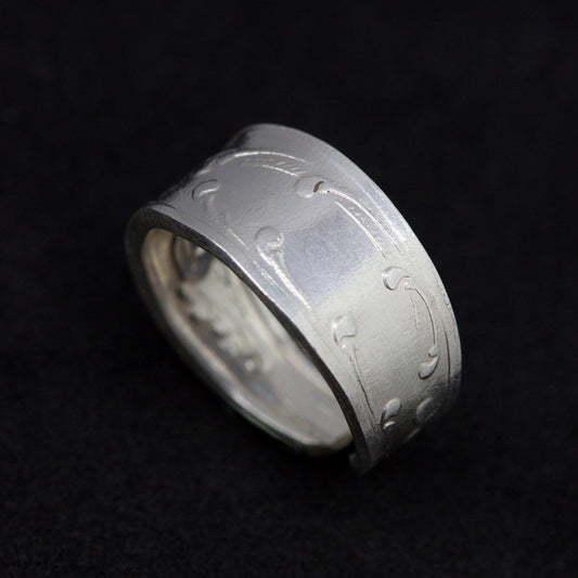 Silver ring with engraved design on a black background